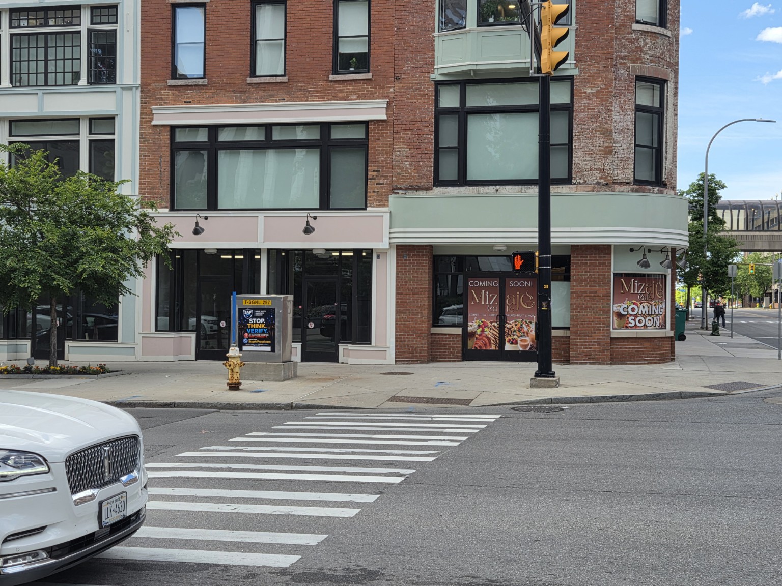 SAF Stop. Think. Verify. public safety sign installed on a traffic signal box at the Main & Clinton intersection in Downtown Rochester, NY — visible to drivers and pedestrians at a busy crosswalk.